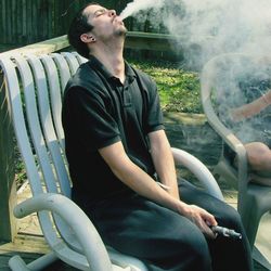 Young man smoking shisha while sitting on chair in yard