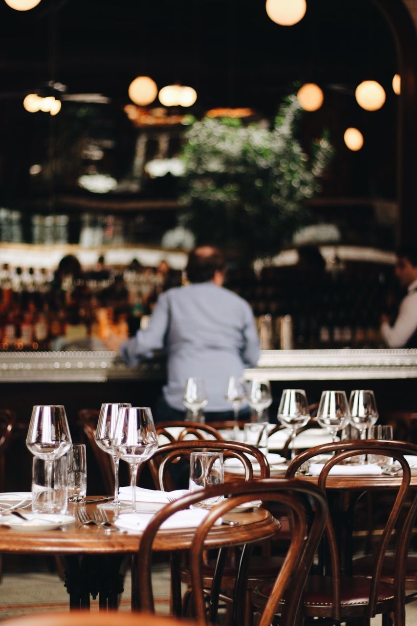 REAR VIEW OF MAN SITTING ON TABLE AT CAFE