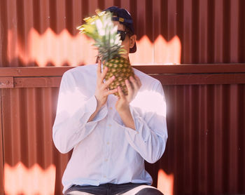 Close-up of young man holding pineapple against corrugated iron