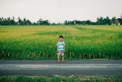 Full length of boy standing on road against field