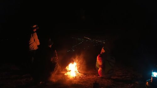 Rear view of people sitting by bonfire at night