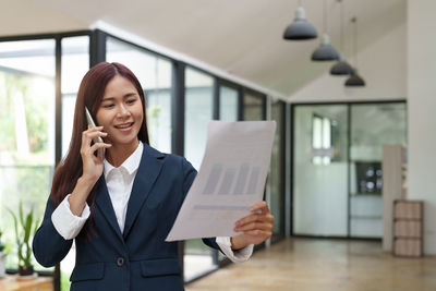 Young businesswoman using mobile phone while standing in office