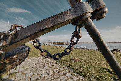 Close-up of rusty chain on railing against sky