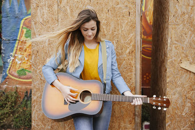 Woman playing guitar while standing by wall