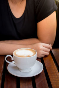 Midsection of woman with coffee cup on table