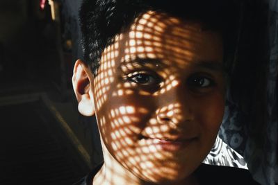 Close-up portrait of smiling teenage boy with sunlight and shadow on face at home