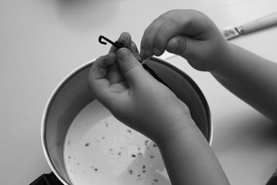 Cropped image of child holding vanilla beans over milk at table