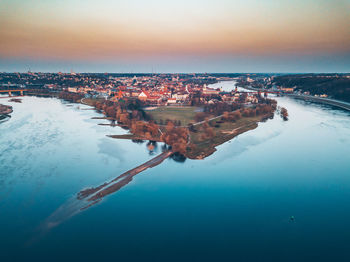 Aerial view of sea by town against sky during sunset