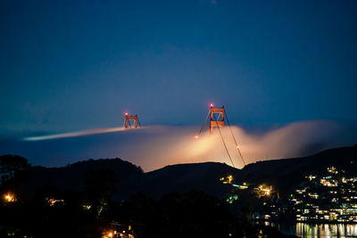 Illuminated bridge over silhouette buildings in city at night