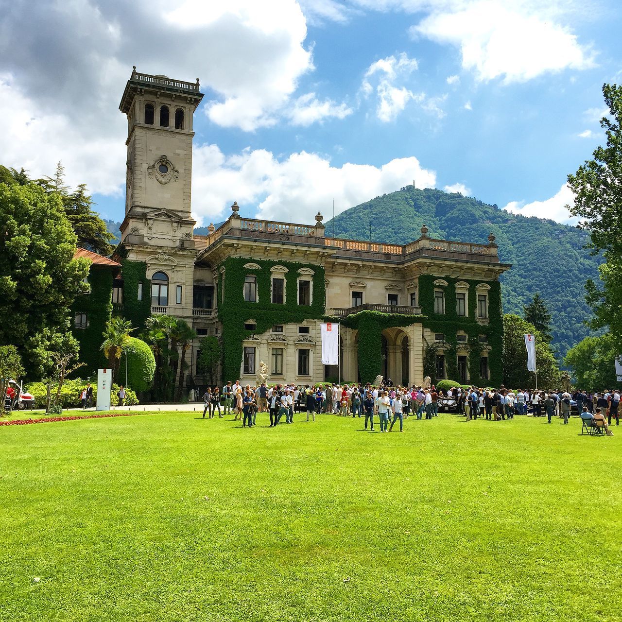 architecture, grass, large group of people, building exterior, built structure, men, sky, person, lifestyles, leisure activity, cloud - sky, lawn, travel destinations, famous place, tourism, tree, tourist, green color, mixed age range