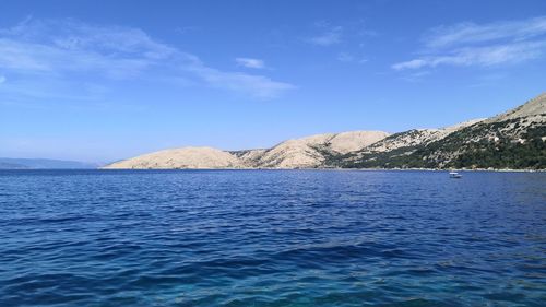 Scenic view of sea by mountain against sky