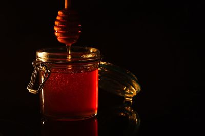 Close-up of honey in jar with dipper over black background