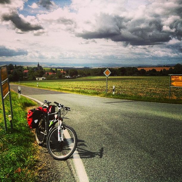 transportation, bicycle, land vehicle, sky, mode of transport, cloud - sky, cloudy, road, grass, parking, field, parked, stationary, landscape, cloud, street, weather, tranquility, the way forward, car