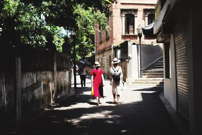 Rear view of women walking on walkway by buildings