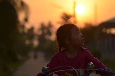 Girl with bicycle against sky during sunset