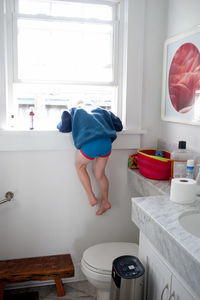Rear view of boy climbing on window in bathroom at home