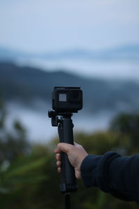 Cropped hand of woman holding camera against field