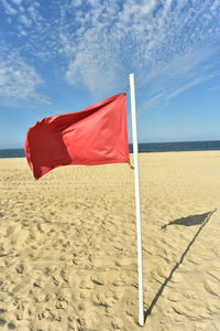 Red flag blowing in wind on flag pole stuck in sand and blue sky background