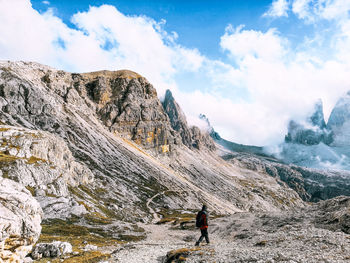 Man walking on rocks by mountains against sky