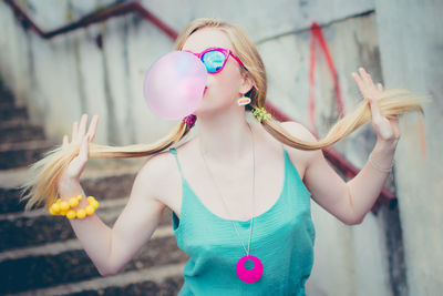 Fashionable young woman holding ponytails while blowing bubble gum