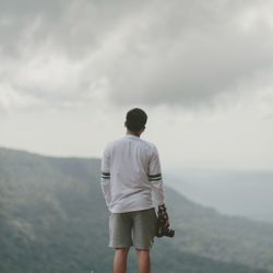 Rear view of man standing on mountain against sky