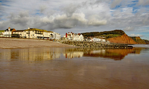 Houses by lake and buildings against sky