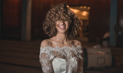 Cheerful young woman with curly hair wearing white evening gown