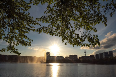 Silhouette buildings by river against sky during sunset