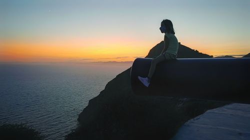 Woman looking at sea against sky during sunset