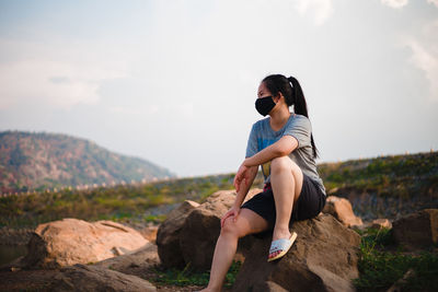 Young woman sitting on rock against sky