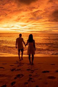 Rear view of women standing on beach against sky during sunset