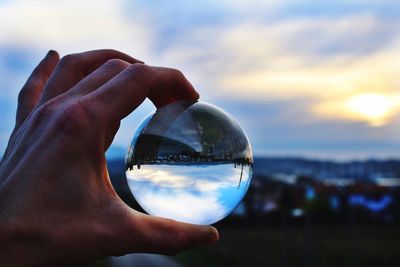 Close-up of human hand holding crystal ball against sky during sunset
