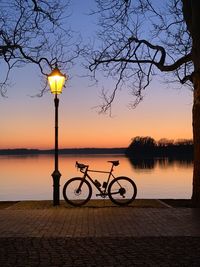 Bicycle on street by lake against sky during sunset