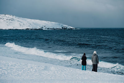 Rear view of people on shore against sky during winter