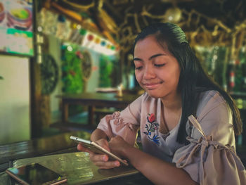 Young woman looking at camera while using mobile phone