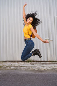 Portrait of smiling young woman jumping against wall