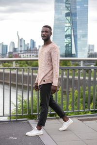 Full length portrait of young man standing against railing in city