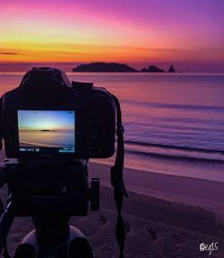 Camera on beach against sky during sunset