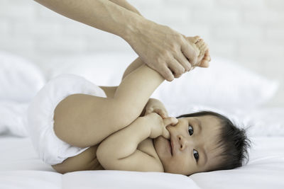 Cropped hand of mother stretching baby on bed at home