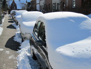 Snow covered cars on road during sunny day