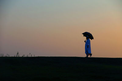 Woman standing on field against clear sky during sunset