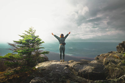 Rear view of woman standing on rock against sky