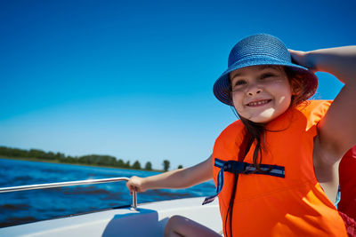 Smiling girl wearing hat standing in boat against sea against clear blue sky