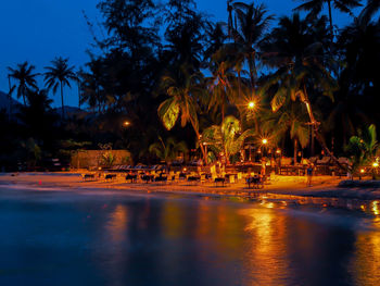 Tables and chairs arranged on illuminated shore at beach