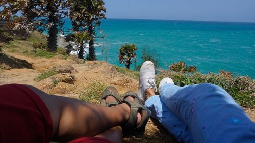 Low section of friends relaxing on sea shore against sky