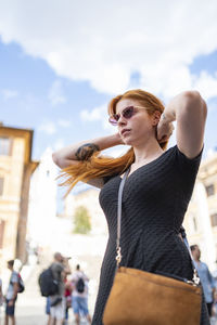 Ginger woman in dress putting tidy her hair in sunny day with blue sky