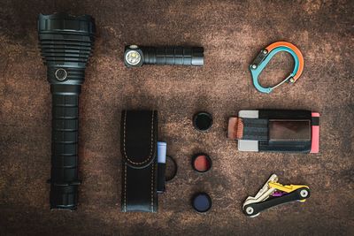 An amount of some edc (everyday carry) items on a wooden surface. there are some flashlights, a clip, a minimalist wallet, 3 flashlight filters, a flashlight cover and a key organizer keychai