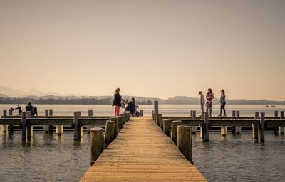 People on pier at lake against sky during sunset