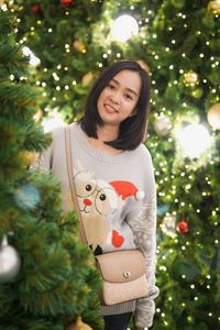 Portrait of young woman standing by christmas tree