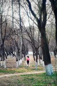 Rear view of woman standing by bare trees